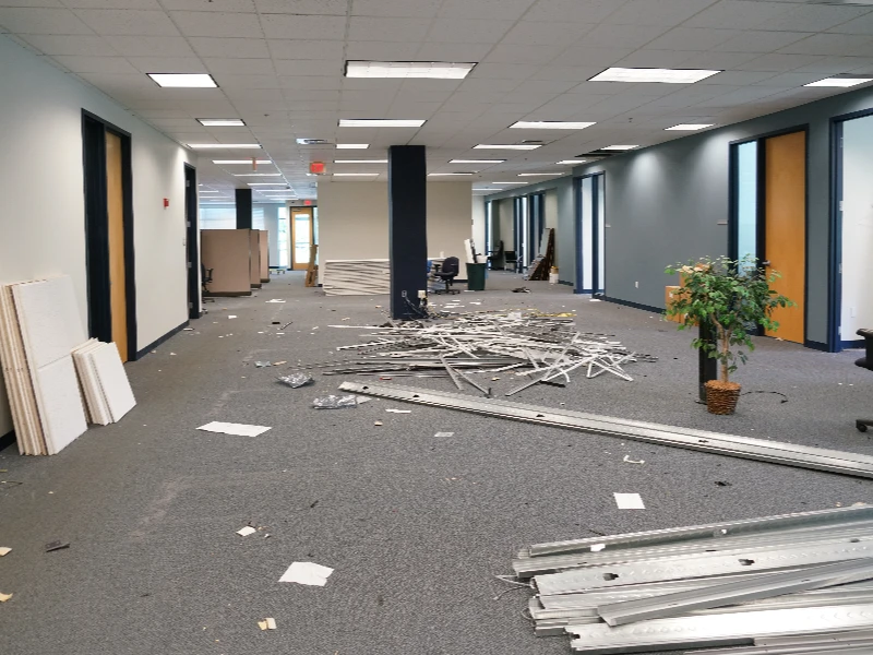 Empty office space with scattered construction debris and a potted plant near the right wall. commercial restoration services