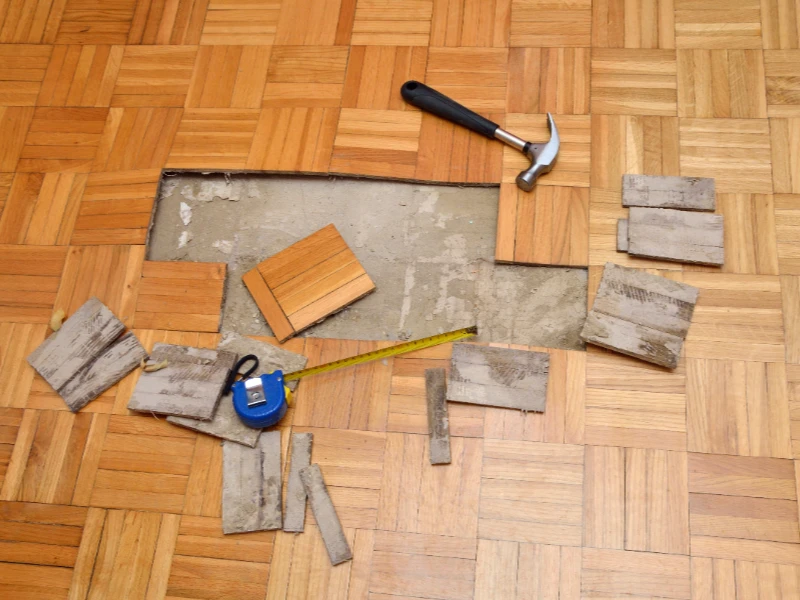 Wooden parquet floor with removed tiles, a hammer, and a measuring tape on top. certified restoration company