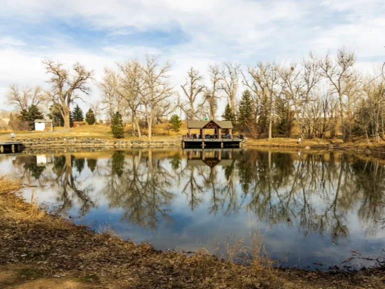 A small wooden pavilion on a dock by a calm pond reflecting leafless trees and a partly cloudy sky. water damage restoration in Highlands Ranch CO