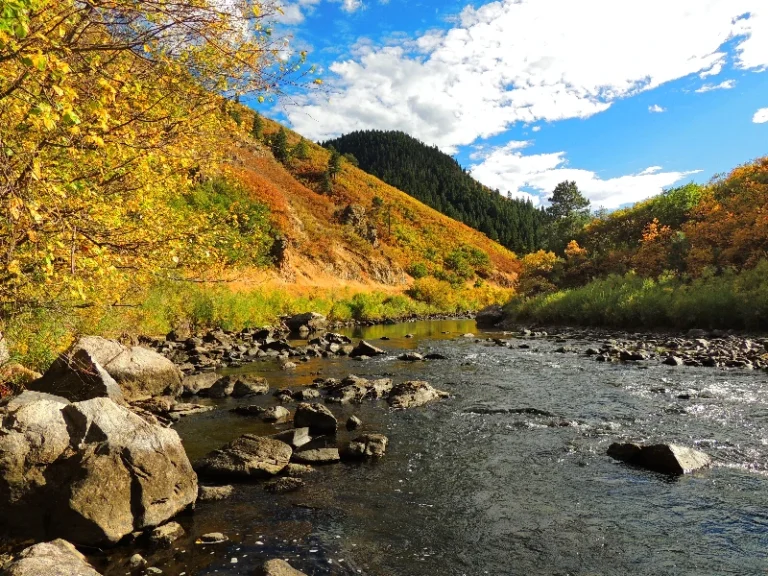 Rocky river flowing through autumn-colored hills under a partly cloudy blue sky. water damage restoration in Littleton CO