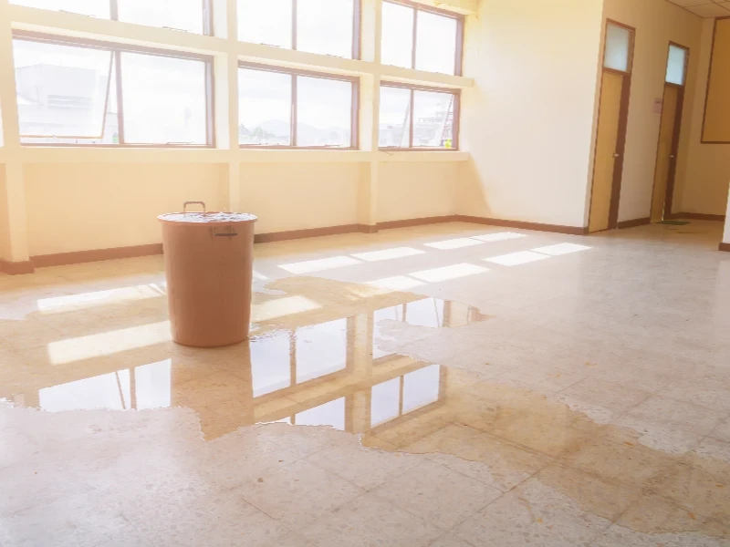 Large water puddle on a tiled floor inside a room with a covered bucket nearby. water damage restoration
